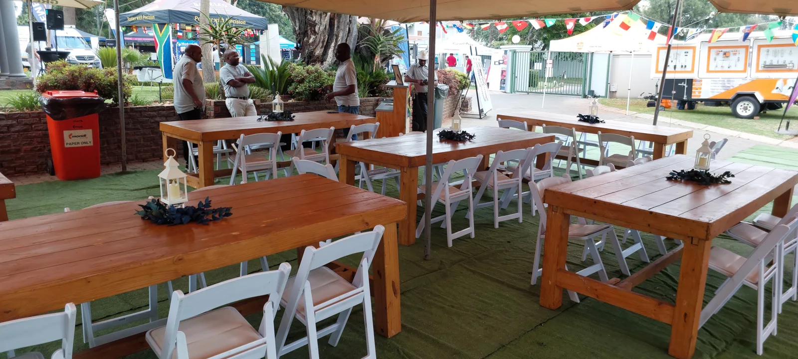 Wooden dining tables and white folding chairs at a decorated garden event