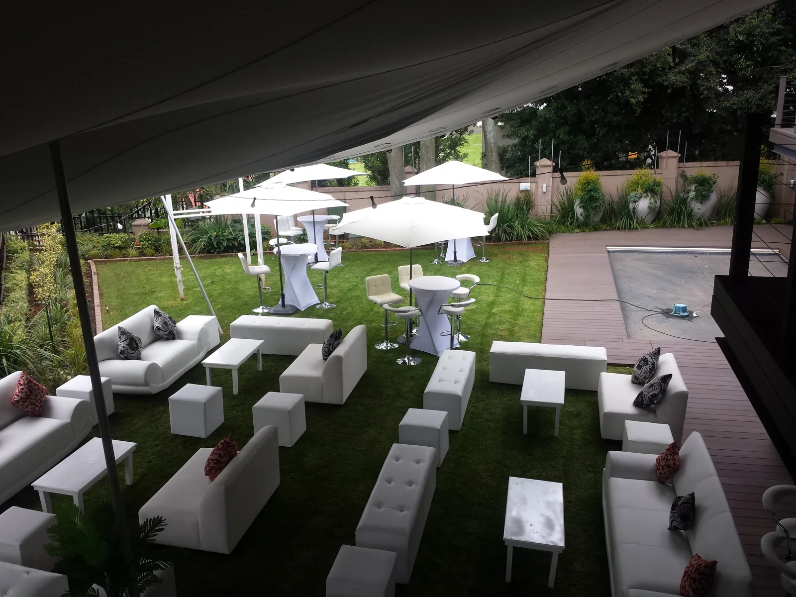 White lounge couches, ottomans and cocktail tables arranged beneath a garden stretch tent
