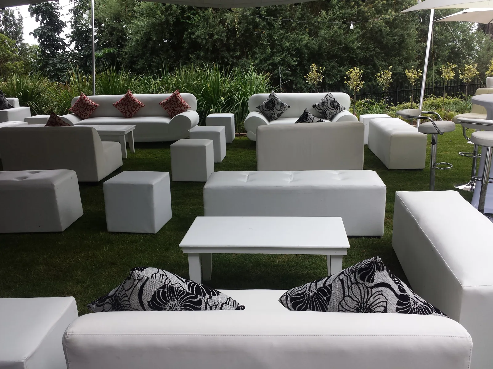 White couches, ottomans and coffee tables arranged on grass with garden umbrellas